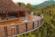 a woman sitting on top of a wooden deck in the middle of trees and mountains