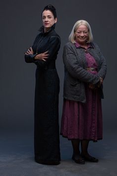 two women standing next to each other in front of a dark background with their arms crossed