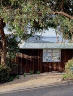 a small wooden house sitting on the side of a road next to trees and bushes