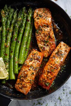 salmon and asparagus in a skillet with lemon wedges