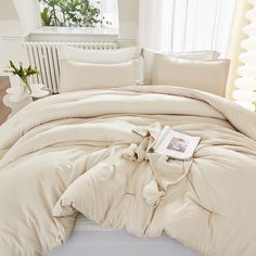 an unmade bed in a bedroom with white walls and curtains, along with a book on the floor