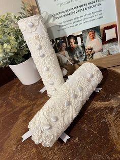 the letter j is made out of white lace and pearled buttons, sitting on a table next to a potted plant