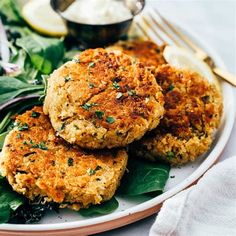 two crab cakes are on a plate with spinach and lemon wedges next to it