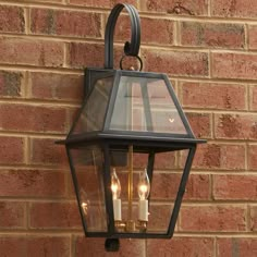 an old fashioned lantern hanging on the side of a brick building with two candles in it