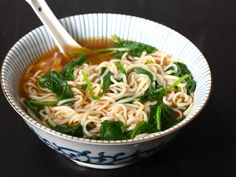 a white bowl filled with noodles and spinach on top of a black countertop