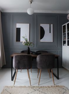 two gray chairs sitting at a wooden table in front of grey paneled walls with pictures on the wall