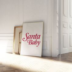 a santa baby sign sitting on top of a hard wood floor next to an open door