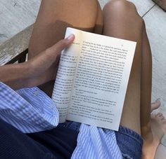 a person sitting on a bench reading a book with their legs crossed and feet propped up