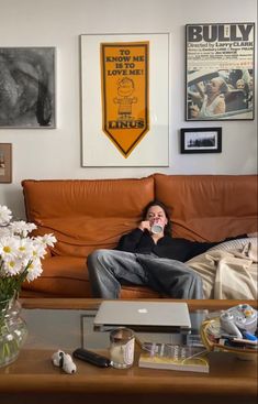 a man sitting on top of a couch next to a table with flowers in front of him