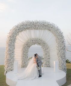 a bride and groom kissing in front of a white floral arch at their wedding ceremony