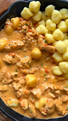 a skillet filled with potatoes and meat covered in gravy on top of a wooden table