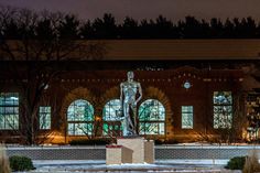 there is a statue in front of the building with many windows and lights on it