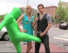 a man and woman standing next to each other in front of a green creature statue