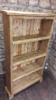 a wooden book shelf sitting on top of a floor next to a stone wall with a brick wall behind it