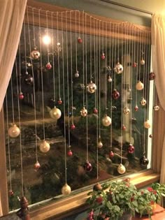 a window with christmas ornaments hanging from it's side and curtains on the outside