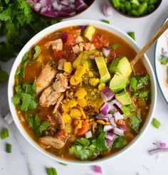 a bowl of chicken tortilla soup with avocado, cilantro and red onion