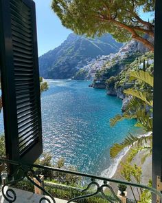 an open window looking out at the ocean and mountains from a balcony with shutters