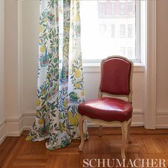 a red chair sitting in front of a window next to a white wall and wooden floor