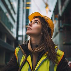 a woman wearing a hard hat and safety vest looking up into the sky in an urban setting