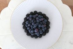 a white plate topped with blueberries and blackberries on top of a wooden table