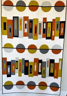 a quilted wall hanging with circles and rectangles in orange, grey, yellow and black