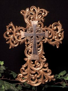 an ornate gold cross with vines around it on a black background in front of leaves