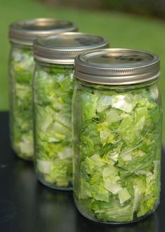 three mason jars filled with lettuce on top of a black table next to grass