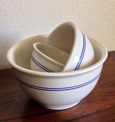 three white bowls stacked on top of each other in front of a wall and wood floor