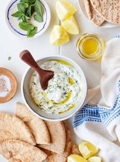 a bowl of dip surrounded by pita chips, lemons and other foodstuffs