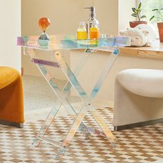 a clear table with bottles and soaps on it in front of a window next to a yellow chair