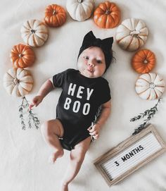 a baby laying on top of a bed next to pumpkins and a sign that says hey boo