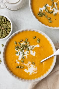 two bowls filled with carrot soup and topped with pumpkin seeds