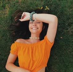 a woman laying in the grass with her hands on her head and wearing a bracelet