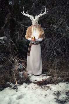 an animal with antlers on it's head is standing in the snow holding fruit