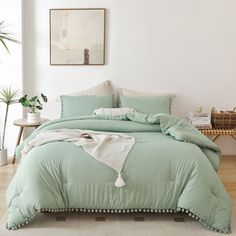 a bed with green comforter and pillows in a room next to a plant on the floor