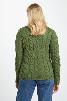 a woman wearing a green cable knit sweater and jeans, looking down at her back