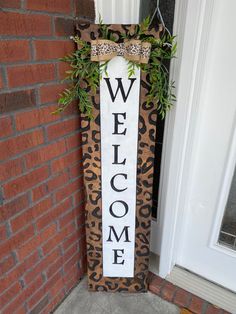 a welcome sign hanging from the side of a door with a plant in front of it