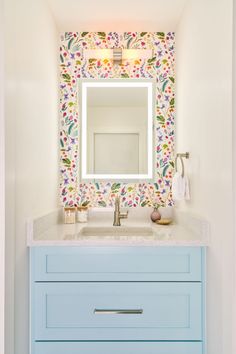 a bathroom vanity with blue drawers and a white sink under a colorful wallpapered mirror