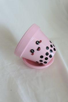 a pink cup with black polka dots on it sitting on a white tablecloth covered surface