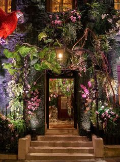 an entrance to a building with lots of flowers and plants on the outside, along with steps leading up to it