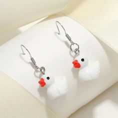 two white ducks with red beaks are hanging from silver earwires on a white surface