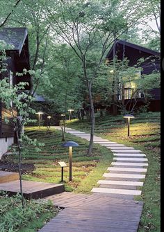 a wooden pathway leading to two cabins in the woods with trees and grass on either side