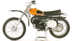 an orange and black dirt bike parked on top of a metal stand in front of a white background