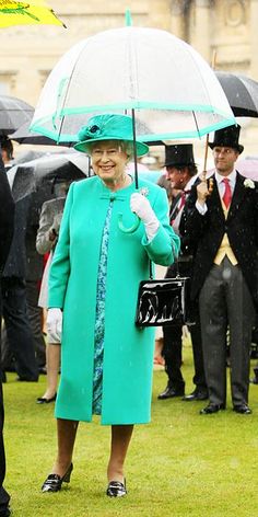 an older woman wearing a green coat and hat holding an umbrella while standing in the rain