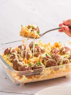 a person scooping some food out of a casserole dish with meatballs and cheese