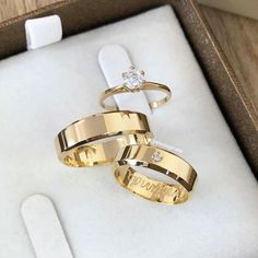 two gold wedding rings in a box with a diamond on the top and an engraved ring on the bottom