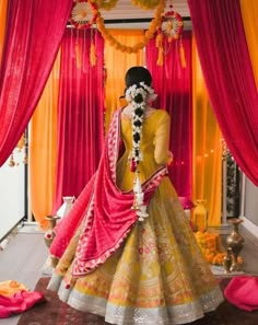 a woman in a yellow and pink lehenga with flowers around her neck, standing on the floor