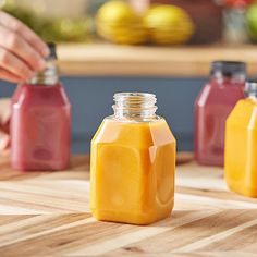 a person is holding a glass bottle with orange juice in it on a wooden table