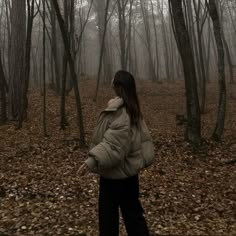 a woman standing in the middle of a forest with trees and leaves on the ground