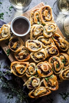 an assortment of pastries on a cutting board next to some glasses and sauces